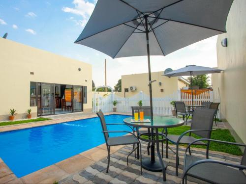uma mesa e cadeiras com um guarda-sol ao lado de uma piscina em Pebble View Luxury Apartments em Lusaka