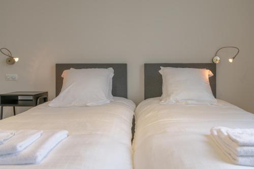 two beds in a room with white sheets and towels at De Vesten Comfort Lodge in Laakdal