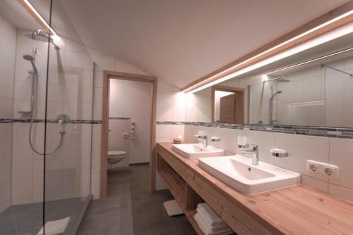 uma casa de banho com 2 lavatórios, um chuveiro e um espelho. em Alpenhof Ferienwohnungen em Oberstaufen