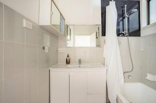 a white bathroom with a sink and a shower at Wollongong station holiday house with Wi-Fi,75 Inch TV, Netflix,Parking,Beach in Wollongong