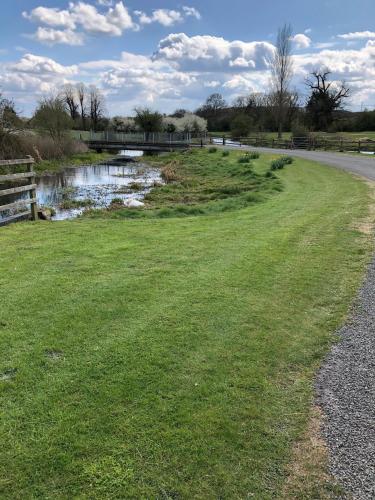 a grassy field next to a river with a bridge at Hyde Mill in Luton