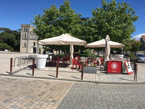 eine Terrasse mit Tischen und Sonnenschirmen vor einem Gebäude in der Unterkunft LA DAME DE COEUR in Soulac-sur-Mer