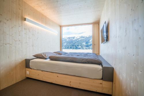a bed in a room with a large window at Revier Mountain Lodge Lenzerheide in Lenzerheide