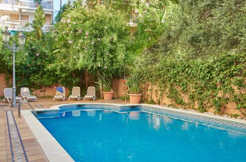 a blue swimming pool with chairs and trees at URH Sitges Playa in Sitges