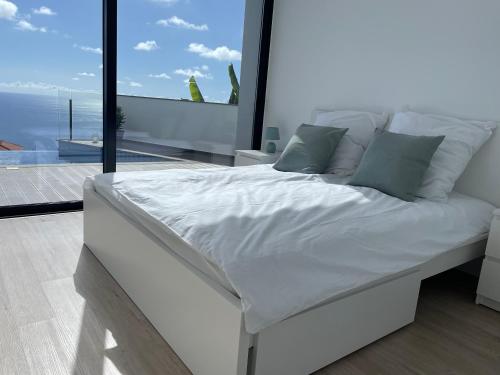 ein weißes Bett in einem Zimmer mit einem großen Fenster in der Unterkunft Villa Sea View in Arco da Calheta