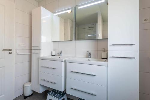 W białej łazience znajduje się umywalka i lustro. w obiekcie Luxe cottage met fietsen, airco & infrarood cabine w mieście Knokke-Heist