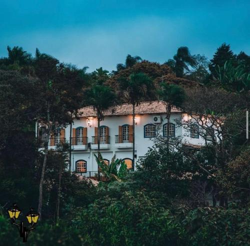 a white building on top of a hill with trees at Confraria Colonial Hotel Boutique in Mairinque
