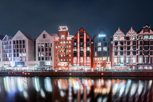 a group of buildings next to a river at night at CLASSY APARTMENTS - Gdańsk - Widok z Wyspy in Gdańsk