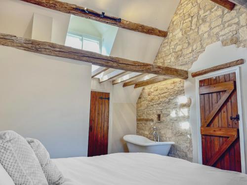 1 dormitorio con pared de piedra, 1 cama y lavamanos en Grooms Lodge, Chipping Campden - Taswell Retreats, en Chipping Campden
