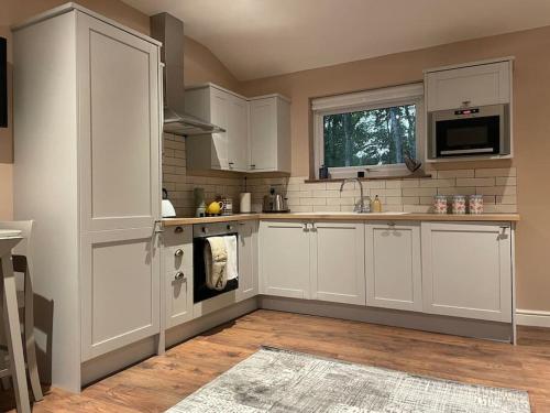 una cocina con armarios blancos y fregadero en Tulip Cottage en Wisborough Green