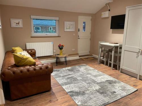 a living room with a leather couch and a table at Tulip Cottage in Wisborough Green