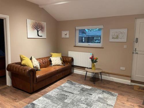 a living room with a brown leather couch and a window at Tulip Cottage in Wisborough Green