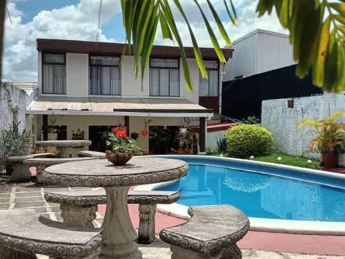 Un patio con mesa y sillas junto a una piscina. en Hotel Casa Tago, en Alajuela