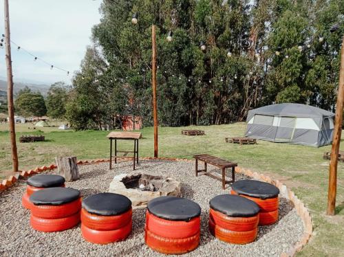 a group of stools around a fire pit with a tent at Camping Las Acacias in Guatavita