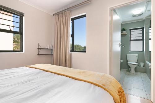 1 Schlafzimmer mit einem weißen Bett und einem Badezimmer in der Unterkunft Serengeti Selfcatering Apartments Tygervalley in Bellville