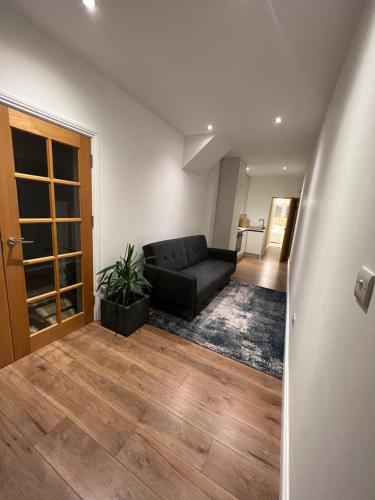 a living room with a black couch and wooden floors at Brand New Modern Flat in Southall