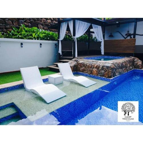 two white chairs and a bed next to a pool at CAMP TREEHOUSE • COTTAGE • POOL • JACUZZI in Antipolo