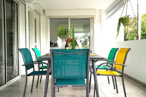 a dining room table with colorful chairs on a porch at Appartement 2 chambres, avec jardin, grande terrasse, Barbecue, 8 min du centre ville in Fort-de-France
