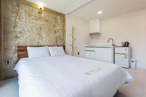 a bedroom with a large white bed and a kitchen at Aewol Oceanstay in Jeju