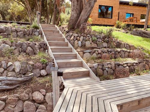 a wooden walkway in a garden with a stone wall at Kingfisher de los Andes in Villa Meliquina
