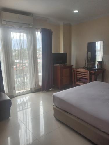 a bedroom with a bed and a television and windows at Hotel Celebes in Manado