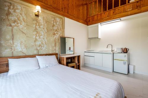 a bedroom with a white bed and a kitchen at Aewol Oceanstay in Jeju