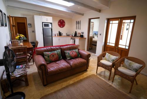 una sala de estar con un sofá de cuero marrón y sillas en Cabriere Cottage en Franschhoek