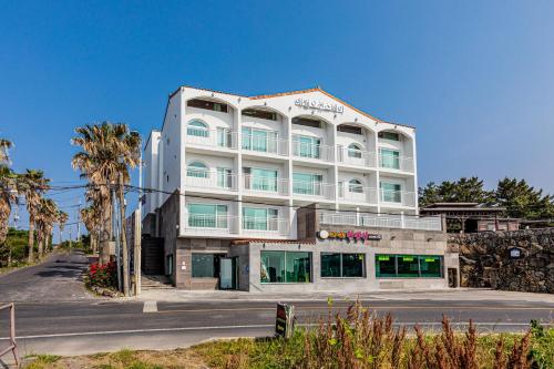 a large white building with palm trees and a street at Aewol Oceanstay in Jeju