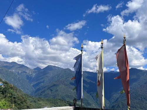 three flags on poles with mountains in the background at The Sherpa's Abode in Gangtok