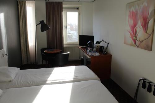 een hotelkamer met 2 bedden en een bureau met een computer bij Fletcher Stadshotel Den Haag in Den Haag
