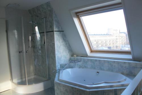 een badkamer met een bad en een douche en een raam bij Fletcher Stadshotel Den Haag in Den Haag