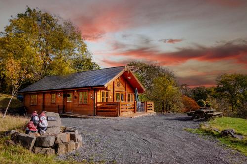 a log cabin with three children sitting in front of it at George Cabin - Log Cabin in Wales with Hot tub in Newtown