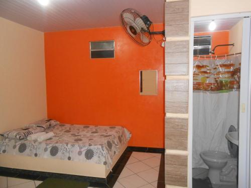 a bedroom with an orange wall and a bed and a toilet at Pousada Salmo 23 in Algodoal