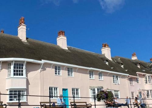 un gran edificio blanco con bancos delante en Benwick Cottage - Beachfront Thatched Cottage set on the marine parade with absolutely spectacular Sea views! Sleeps 4, en Lyme Regis