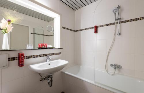 La salle de bains blanche est pourvue d'un lavabo et d'une baignoire. dans l'établissement Leonardo Hotel Hamburg Elbbrücken, à Hambourg