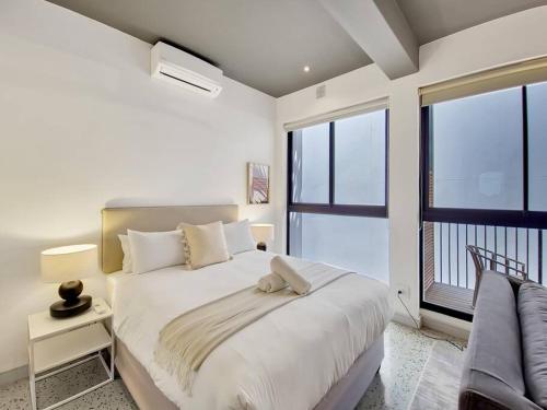 a white bedroom with a bed and a large window at Brand new, luxury, wifi, pool with 24hr security in Cape Town