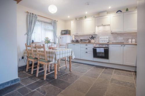 a kitchen with white cabinets and a table and chairs at Fferm-Llong Cottage Ship Farm - 2 Bedroom -Rhossili in Rhossili
