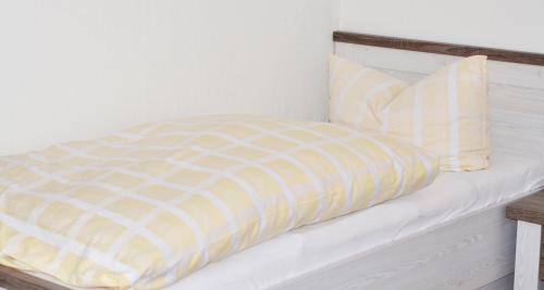a bed with a yellow and white comforter and two pillows at Hotel Pension Petra in Bad Zwischenahn