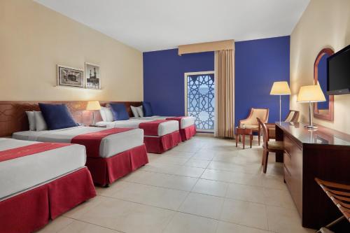 メッカにあるMakarem Al Bait Al Azizia Hotelのベッド3台とテレビが備わるホテルルームです。