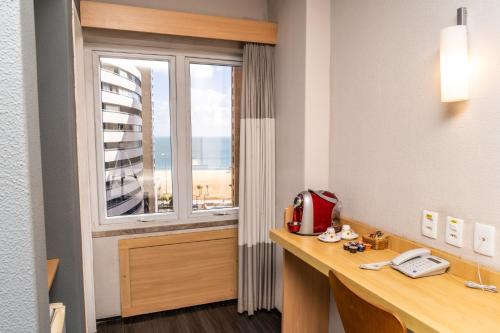 a room with a window and a desk with a phone at ibis Fortaleza Praia de Iracema in Fortaleza