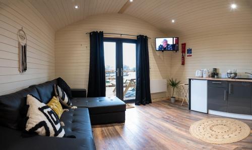ein Wohnzimmer mit einem schwarzen Sofa und einer Küche in der Unterkunft The Buzzard - 6 Person Family Glamping Cabin in Dungarvan