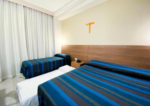 a hotel room with two beds and a cross on the wall at Hotel Rainha do Brasil in Aparecida