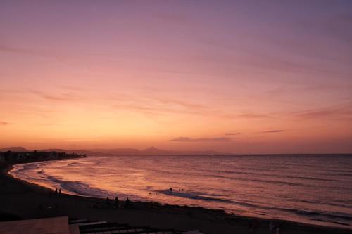 a beach at sunset with people in the water at Hotel Noguera Mar in Denia