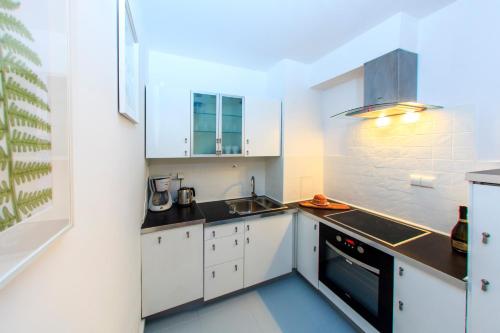 cocina con armarios blancos, fregadero y fogones en Comfy Apartment Dobra 54, en Varsovia
