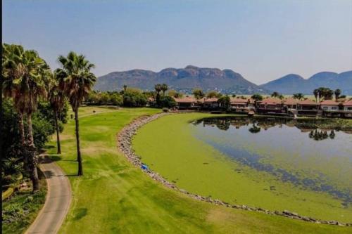 a park with a lake and palm trees and mountains at Pecanwood villa on Hartbeespoort Dam in Hartbeespoort