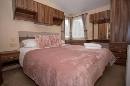 a bedroom with a large bed with a pink blanket at Willow View - Hoburne Cotswolds Holiday Park in South Cerney