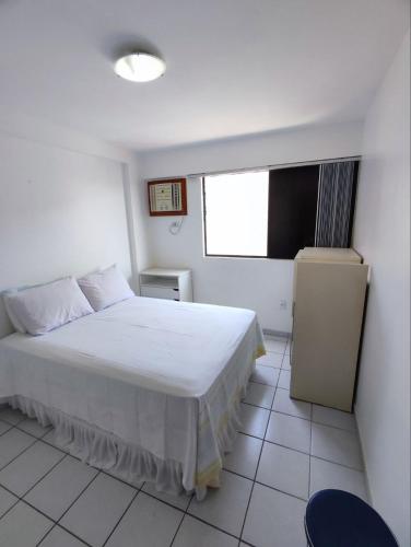 um quarto com uma cama branca e uma janela em Apartamento com piscina a uma quadra da praia de jatiuca em Maceió