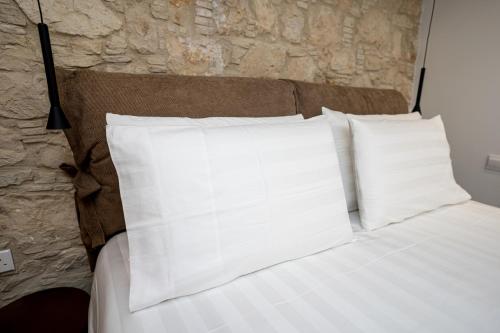 a bed with white pillows and a stone wall at Palazzino Luxury Suites in Lofou