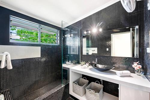 La salle de bains est pourvue de carrelage noir, d'un lavabo et d'un miroir. dans l'établissement Cool by the Pool - A Private Beachside Retreat, à Fannie Bay