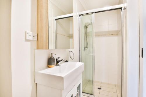 La salle de bains blanche est pourvue d'un lavabo et d'une douche. dans l'établissement Hayes Beach House I Award Winner I 4 Mins to Beach, à Callala Beach
